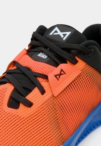 Sportssko med en lys orange mesh-overdel og sorte detaljer, sikre sorte snørebånd og en struktureret blå sål. Gummiseret branddetalje inkluderet.
