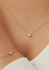 Goldkette und Armband mit einem zentralen runden klaren Edelstein, zarten Ketten und einer glatten Textur auf der Haut.