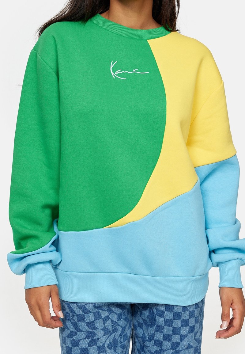 Sweat-shirt coloré avec des panneaux verts, jaunes et bleus. Matière douce, coupe oversize, encolure ronde et poignets côtelés. Détail avec logo signature.
