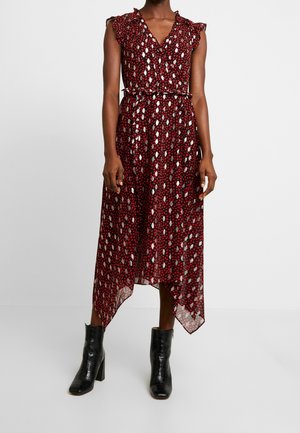 Robe rouge sans manches avec des taches abstraites blanches et noires, encolure en V à volants, ourlet en pointes, portée avec des bottines noires.