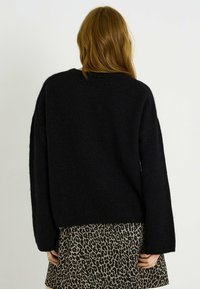Pull noir surdimensionné en tissu doux et texturé. Caractérisé par des manches larges et une coupe décontractée, porté avec une jupe imprimée léopard.