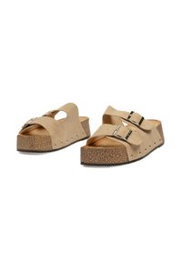 Sandalias de plataforma beige hechas de suave ante. Cuentan con dos hebillas ajustables, diseño recortado y suela texturizada marrón con tachuelas plateadas.