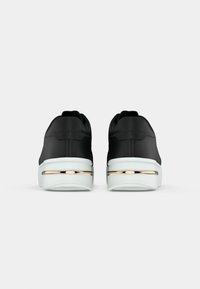 Czarne sneakersy z białymi podeszwami i złotymi paskami akcentującymi, pokazane od tyłu na jednolitym białym tle.