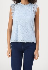 Ljusblå spetsblus med scallop-formad halsringning och ärmslut, som har blommönster och en något lös passform. Bärs tillsammans med mörkblå jeans.