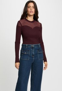 Haut à manches longues côtelé bordeaux avec des accents rayés transparents sur les épaules, associé à un jean large taille haute bleu foncé avec poches.