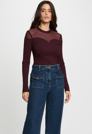 Haut à manches longues côtelé bordeaux avec des accents rayés transparents sur les épaules, associé à un jean large taille haute bleu foncé avec poches.