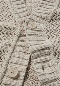 Beige gestrickte Strickjacke mit einem strukturierten Muster, geripptem Kragen und zwei runden Knöpfen vorne. Weiches, leichtes Material.