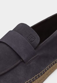 Mocassin en daim gris foncé avec une large bride sur le devant et des détails de semelle cousue à la corde.