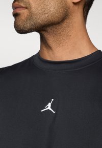 Μαύρο αθλητικό t-shirt με στρογγυλή λαιμόκοψη και κοντά μανίκια, με λευκό λογότυπο Jordan στην αριστερή πλευρά του στήθους. Λείο υφή.