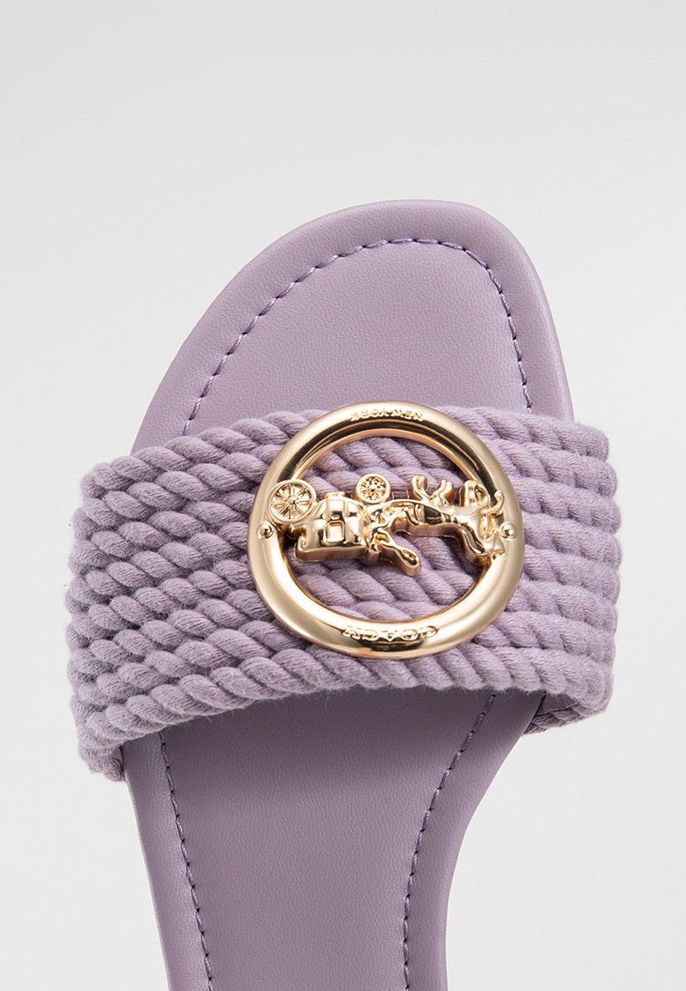 Fioletowe klapki z plecionym paskiem, złotą okrągłą klamrą i gładką podeszwą. Miękka tekstura i zaokrąglony kształt.