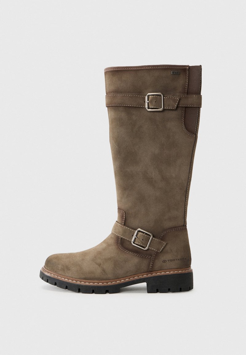 Botte en suède marron, haute, avec une texture lisse, des détails avec boucle et une semelle en caoutchouc. Présente des coutures renforcées et un design droit et vertical.