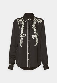 Blusa in satin nero con motivi floreali ricamati bianchi e fiocchi, con chiusura a bottoni e rifiniture a contrasto sul colletto e sui polsini.