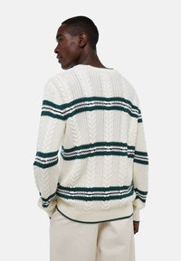 Pull en maille torsadée couleur crème avec des rayures horizontales vertes et blanches. Présente un col rond et une coupe décontractée. Le fil texturé ajoute de la profondeur.