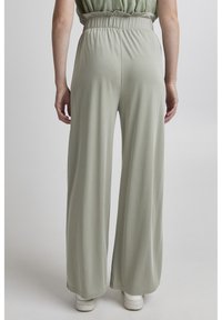 Light green, flowy wide-leg pants with an elastic waist. Made of soft fabric, designed for comfort. Worn with white sneakers.