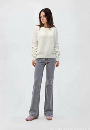 Cremfarbener Strickpullover mit geripptem Muster, graue Schlagjeans und rosafarbene Slipper. Mit Knöpfen am Kragen und lässiger Passform.