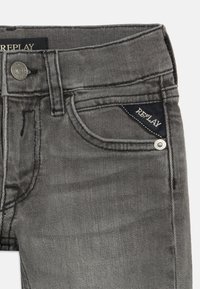 Grå denimjeans med klassisk fem-lomme-design, sølvfarget hardware og en merket mørk lapp i fronlommen.
