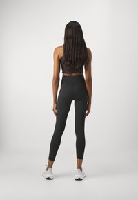 Black athletic leggings with a high waist and snug fit, paired with a black cropped top. Worn with white athletic shoes, long wavy hair.