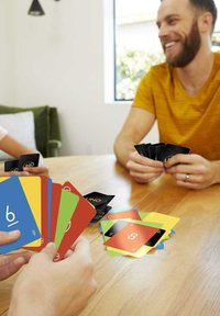 UNO card game in vibrant colors: blue, yellow, red, green. Cards feature numbers and symbols. Wooden table, casual setting.