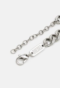 Silver metal chain bracelet featuring oval links, a textured center plate with "DIESEL" engraving, and a lobster clasp for fastening.
