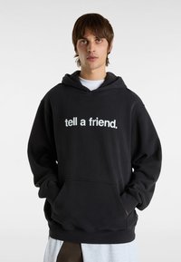 Hørnesvart hoodie til mænd med en frontlomme, ribbede manchetter og teksten "fortæl en ven." trykt i hvidt på brystet. Blødt stof.
