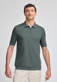 Mörkgrön kortärmad polo med dragkedja i kragen och en liten logotyp på bröstet; slät textur och figursydd design.