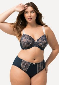 Bügel-BH und Panty-Set in Marineblau mit beigen Akzenten. Der BH hat eine florale Spitzen-Overlay, verstellbare Träger und ein Schleifendetail. Die hochgeschnittene Panty passt im Design dazu.