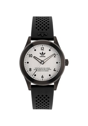 Montre en caoutchouc noir avec un bracelet perforé, cadran métallique gris, marqueurs d'heure noirs, et détail du logo à 12 heures.