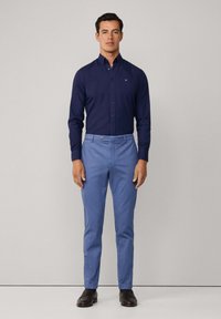 Marineblauwe blouse met lange mouwen en kraag, gecombineerd met lichtblauwe op maat gemaakte broek en donkere schoenen. Minimalistisch ontwerp.
