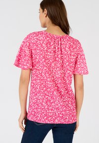 Top corto a maniche corte rosa floreale con una vestibilità ampia e scollatura arricciata, caratterizzato da un motivo di fiori bianchi su un tessuto morbido.