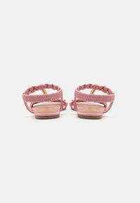 Pink braided sandals with a flat sole, featuring ankle straps and a smooth tan insole. The straps are intricately woven for added detail.