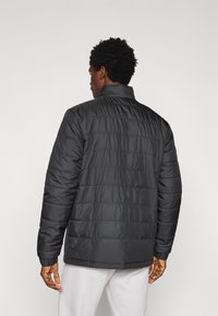 Μαύρο μπουφάν τύπου puffer με οριζόντιες ραφές, ψηλό γιακά και ριμπ μανσέτες. Ελαφρύ υλικό, που προσφέρει λεία, γυαλιστερή υφή.