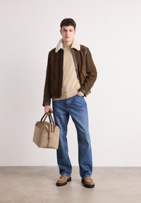 Brun semsket jakke med shearling-krage, beige genser, blå jeans og brun veske. Brune sko med en robust såle fullfører antrekket.