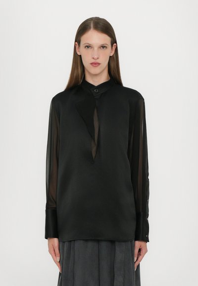 Chemise noire à manches longues avec un col à boutons, des manches transparentes et une patte de boutonnage décalée. Tissu lisse avec une finition élégante.