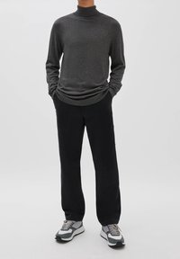 Grijze coltrui gecombineerd met zwarte broek. Schoenen hebben grijze en witte accenten. Zachte textuur, ontspannen pasvorm, casual ontwerp.