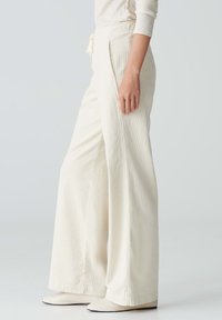 Wijduitlopende broeken in crème, gemaakt van textuurovergoten stof. Elastische tailleband met trekkoord. Te combineren met puntige schoenen.
