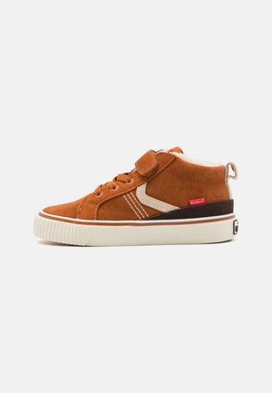 Baskets montantes en daim beige avec des coutures blanches, des accents beige, une sangle Velcro et une semelle en caoutchouc arborant un logo rouge.