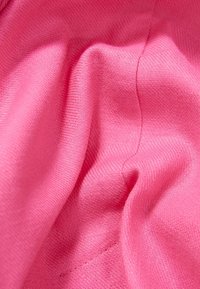 Tela rosa con una textura suave, que presenta un patrón tejido. La tela arrugada muestra sutiles variaciones en el tono y la estructura de las fibras.