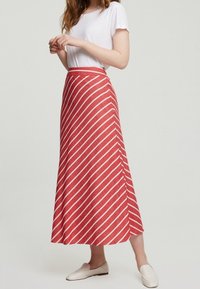 Jupe midi rouge avec des rayures diagonales blanches, fabriquée en tissu léger. Présente une taille ajustée et une silhouette évasée.