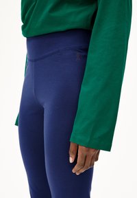 Navy blauwe leggings met een hoge tailleband, voorzien van een klein bruin logo. Gecombineerd met een groene longsleeve top met een zachte textuur.