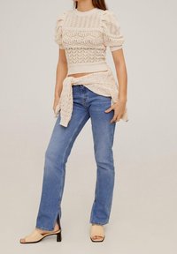 Knit sweater in cream with puff sleeves and intricate patterns, paired with light blue jeans and beige block-heeled sandals.
