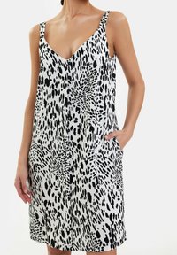 Vestido sin mangas de estampado de leopardo en blanco y negro con escote en V, cierre de botones en la parte delantera y bolsillos laterales, hecho de una tela texturizada.