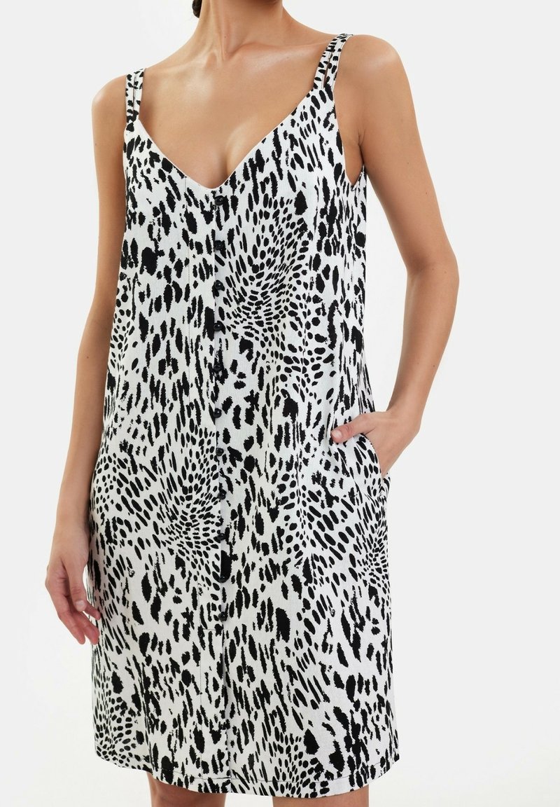 Vestido sin mangas de estampado de leopardo en blanco y negro con escote en V, cierre de botones en la parte delantera y bolsillos laterales, hecho de una tela texturizada.
