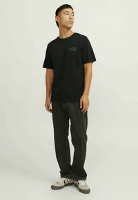 Μαύρο βαμβακερό T-shirt με κοντά μανίκια και μικρό λογότυπο μπροστά, συνδυασμένο με σκούρες τζιν και γκρίζα παπούτσια με λευκές λεπτομέρειες.