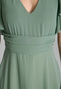 Groene jurk met een diepe V-hals, korte flapmouwen en een getailleerde tailleband. Gemaakt van zachte stof, met een gladde textuur en een vloeiende silhouette.