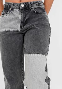 Schwarze und graue Jeans mit einem Patchwork-Design und auffälligen Farbbereichen, im Fünf-Taschen-Stil und mit Knopfverschluss.