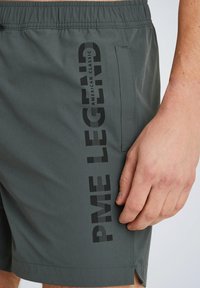 Pantaloni da spiaggia grigi realizzati in tessuto leggero, con una stampa del logo verticale nera sul lato e una tasca laterale con un design a fessura.