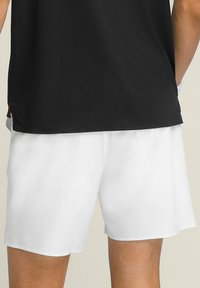 Pantalones cortos deportivos blancos con una textura suave, que cuentan con una cinturilla elástica. Combinados con una camiseta negra para crear contraste.