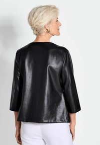 Zwarte leren top met een iets glanzende textuur, driekwart mouwen en een ronde halslijn, met een ontspannen pasvorm en strakke lijnen.