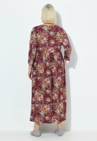 Largo vestido burdeos con patrón floral en tonos de rosa y azul, mangas tres cuartos y falda acampanada. Lleva zapatos azul claro.