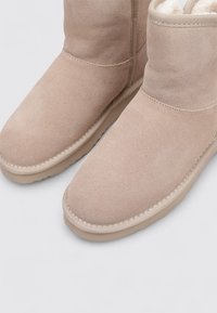 Botines de ante beige con forro de piel suave, punta redonda y borde cosido. Cuenta con una suela de goma flexible para agarre y comodidad.